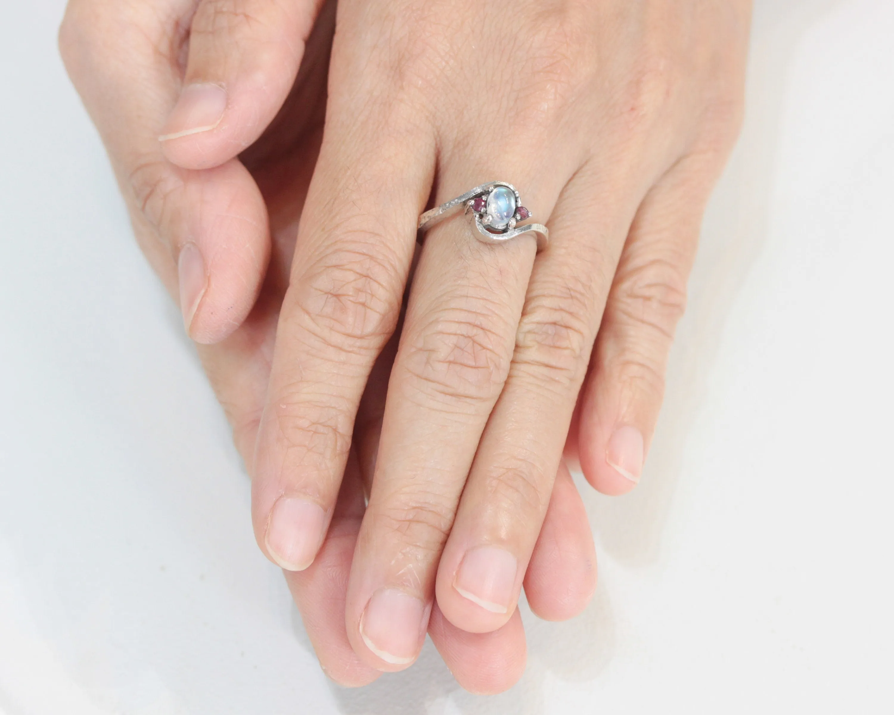 Oval cabochon moonstone ring with tiny ruby side set gems in prongs setting with sterling silver oxidized texture band