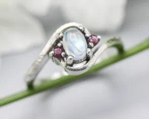 Oval cabochon moonstone ring with tiny ruby side set gems in prongs setting with sterling silver oxidized texture band